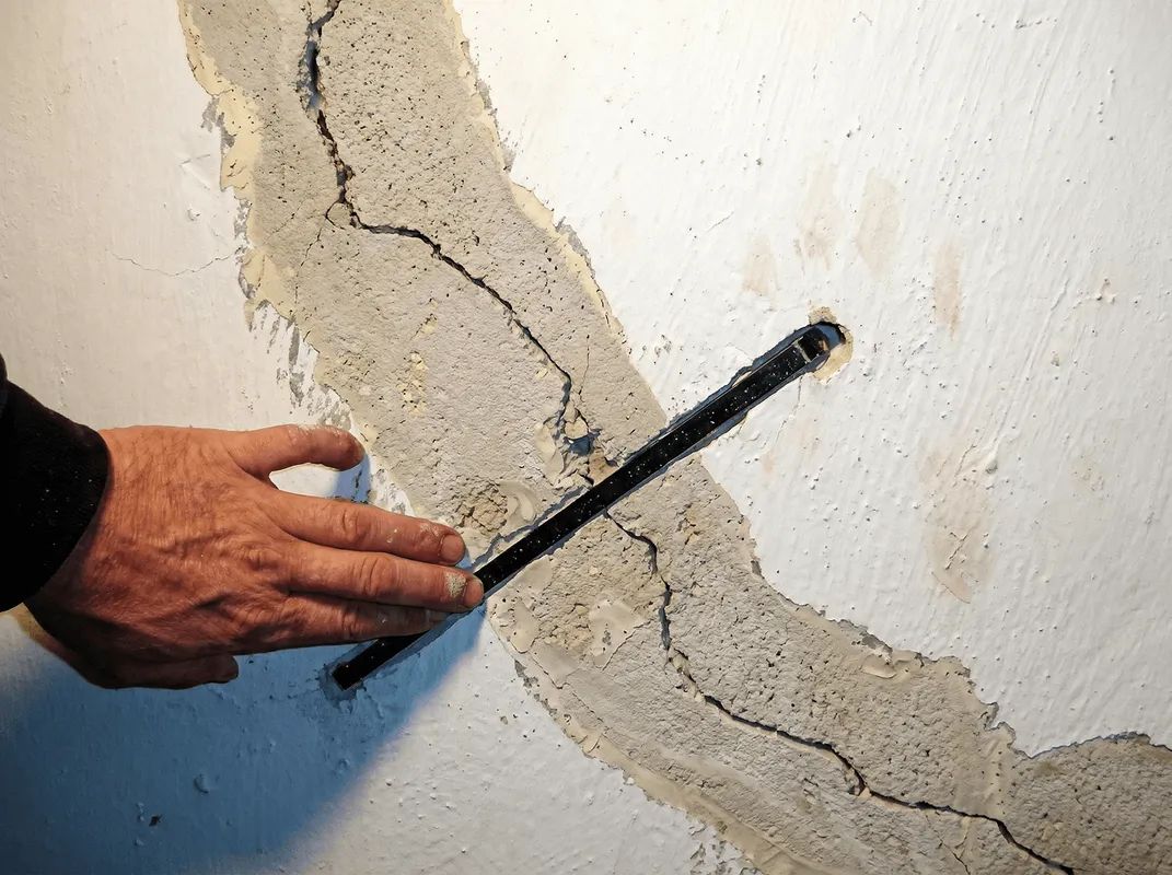 A wall with a large crack is being inspected by a professional in Mesa, AZ